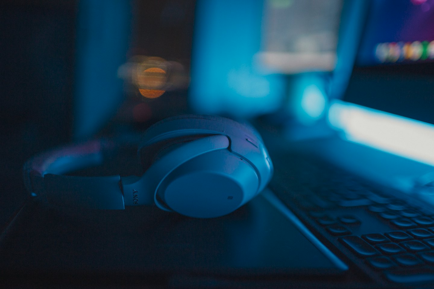 Wireless headphones on a laptop keyboard with blue light.