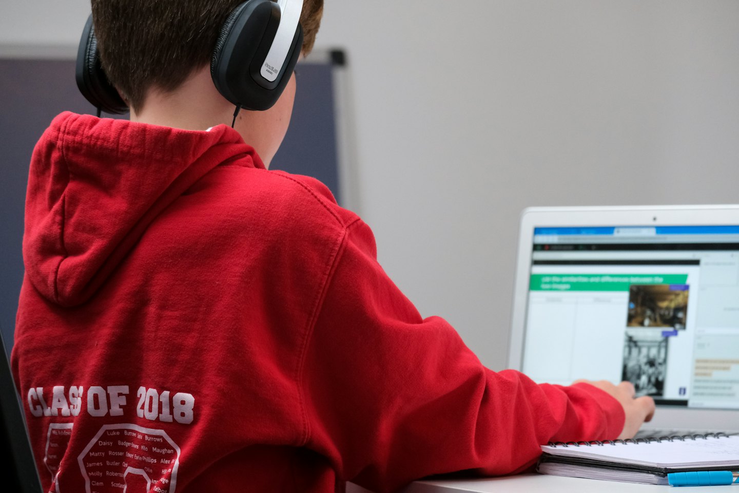 Person in red hoodie with headphones studies on a laptop.